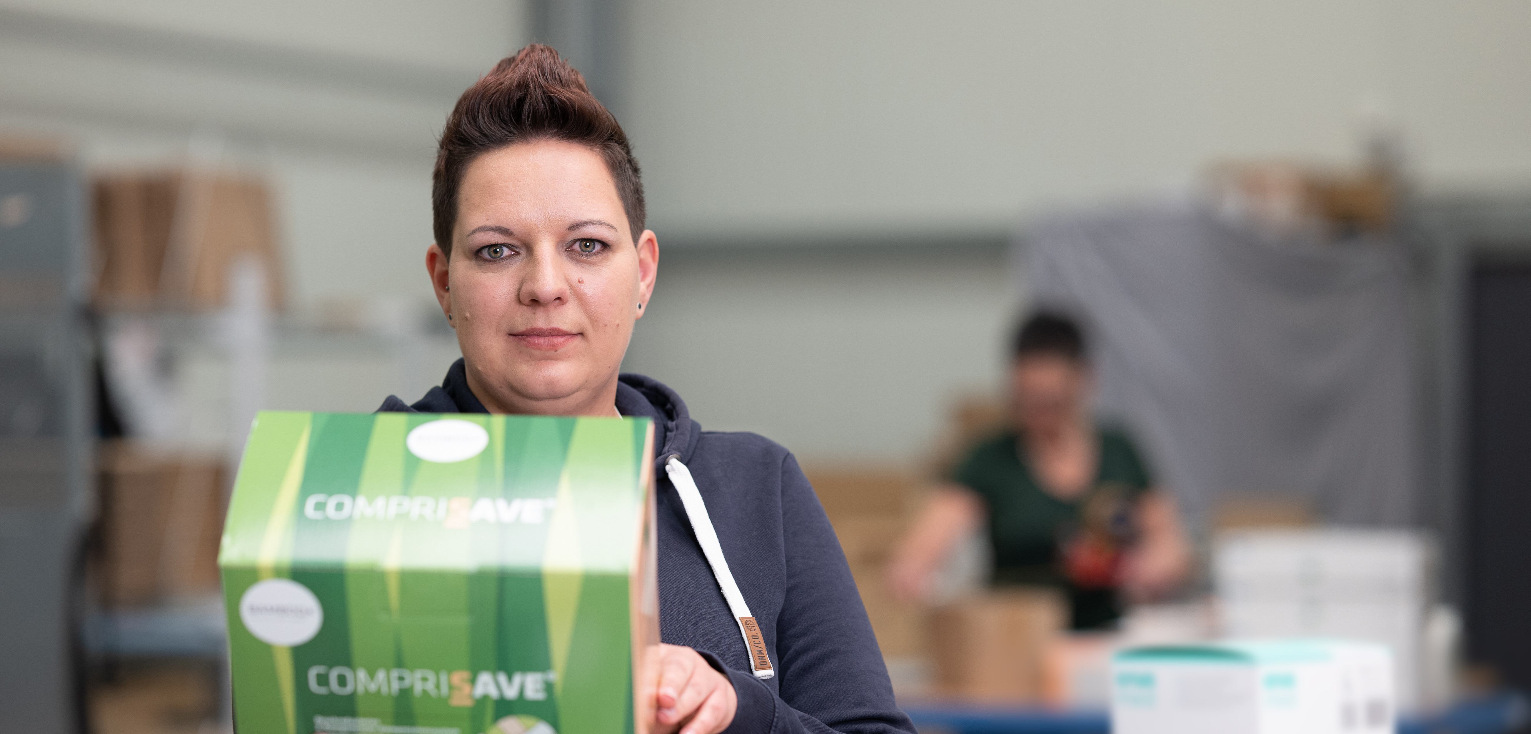 Unsere den Betrachter fokussierende Mitarbeiterin Heike hält im Lager eine Packung CompriSave in die Kamera. | © Bamboo Health Care GmbH