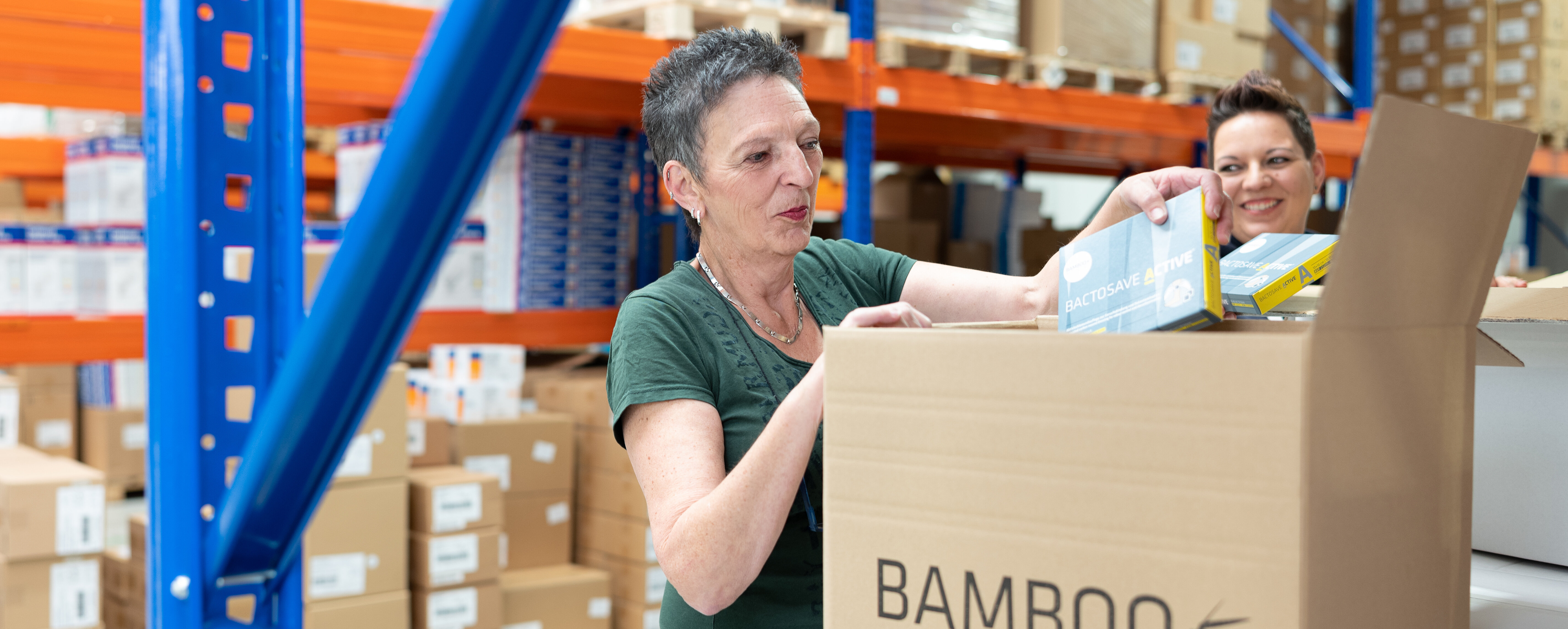 Unsere lächelnden Mitarbeiterinnen Michaela und Heike, die im Lager unser Produkt BactoSave Active® in einen Bamboo Versandkarton packen. | © Bamboo Health Care GmbH