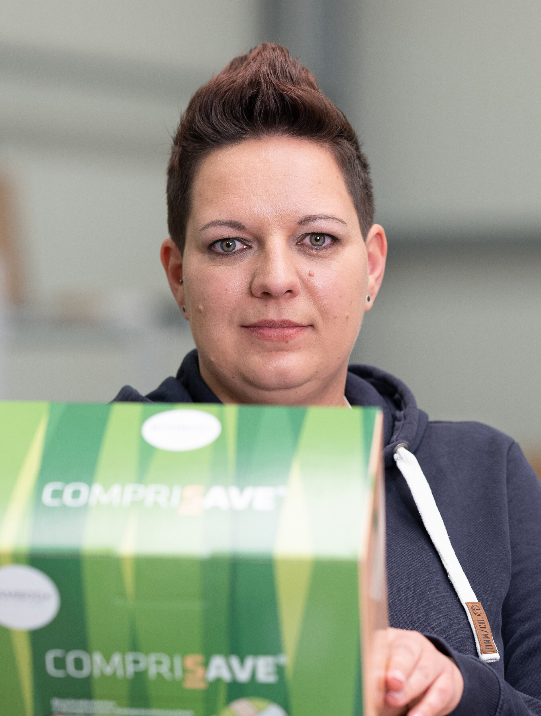 Unsere den Betrachter fokussierende Mitarbeiterin Heike hält im Lager eine Packung CompriSave in die Kamera. | © Bamboo Health Care GmbH