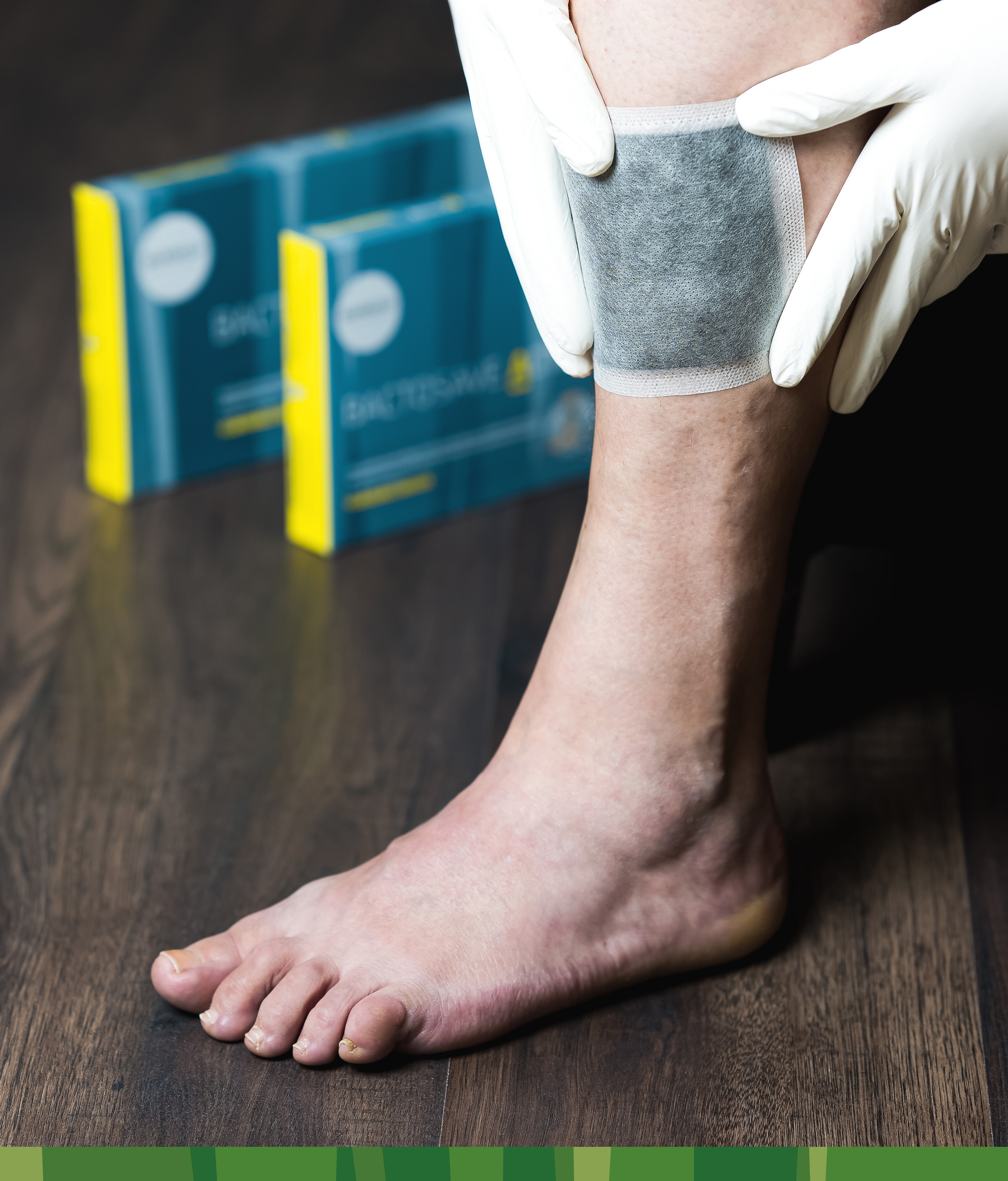 Bein mit applizierter BactoSave Active® Aktivkohlewundauflage mit beiden Verpackungsgrößen im Hintergrund. | © Bamboo Health Care GmbH