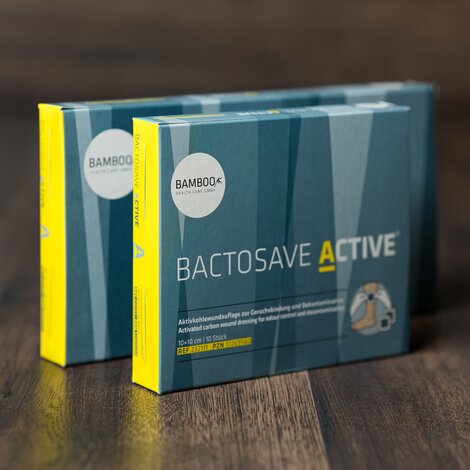 Die zwei Verpackungsgrößen von BactoSave Active® stehend auf einem dunklen Holzboden. | © Bamboo Health Care GmbH