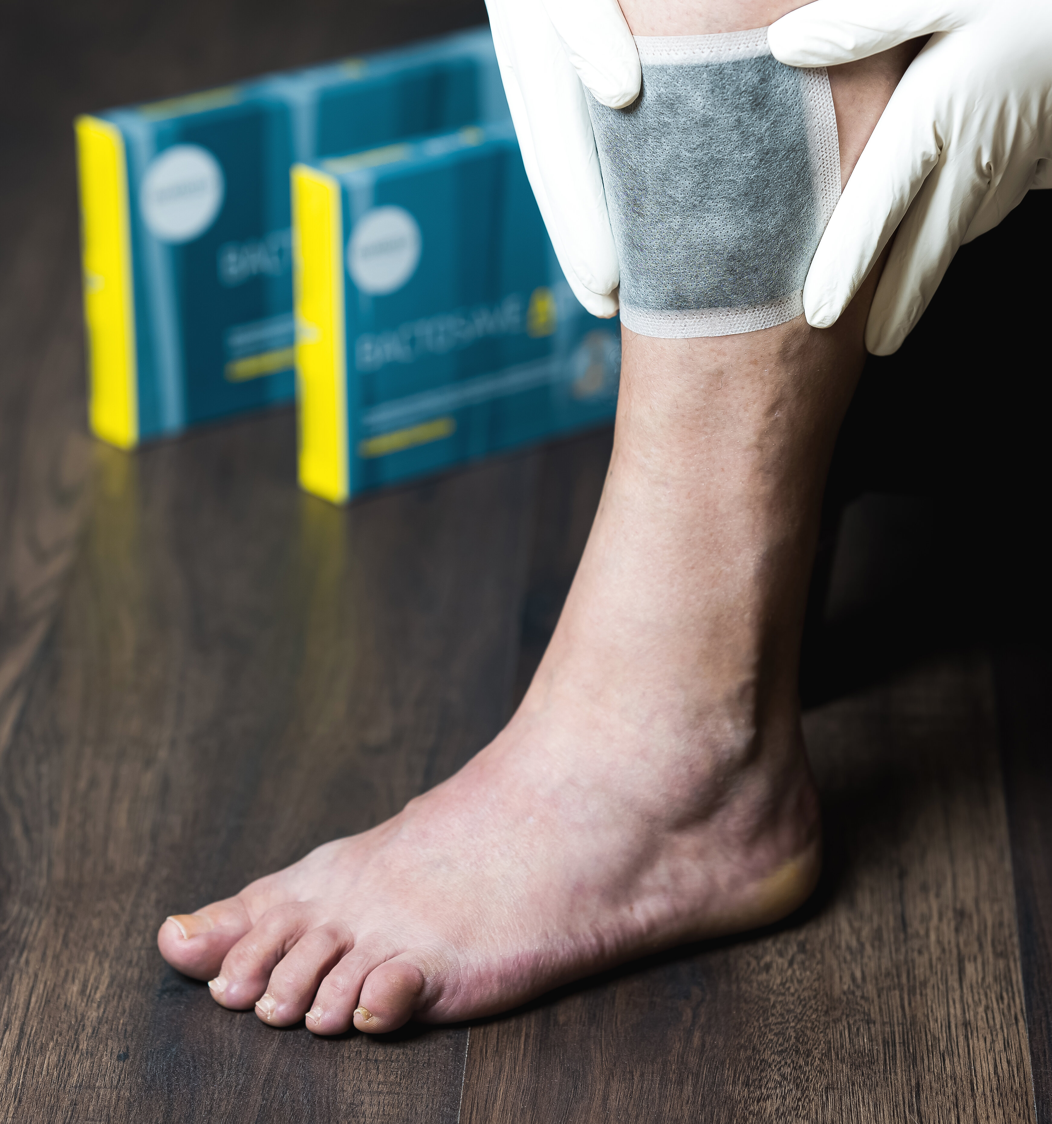 Bein mit applizierter BactoSave Active® Aktivkohlewundauflage mit beiden Verpackungsgrößen im Hintergrund. | © Bamboo Health Care GmbH
