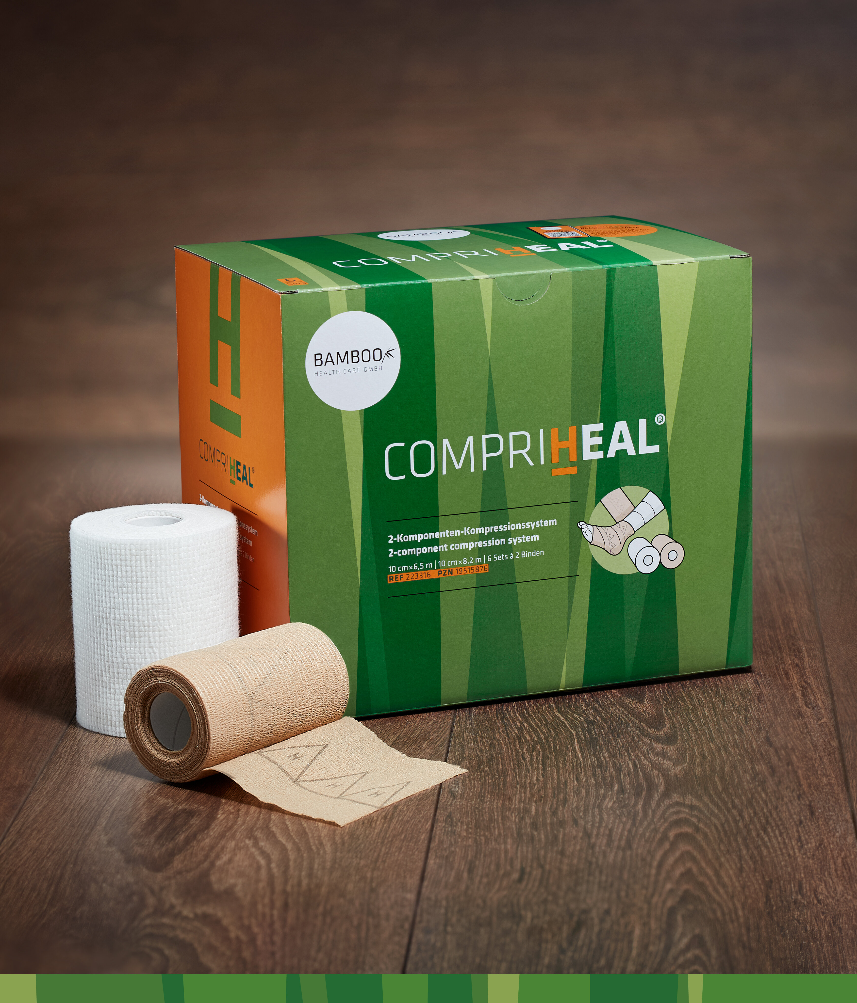 Die Verpackung von CompriHeal® stehend mit einem Set Kompressionsbinden im Vordergrund auf einem dunklen Holzboden. | © Bamboo Health Care GmbH