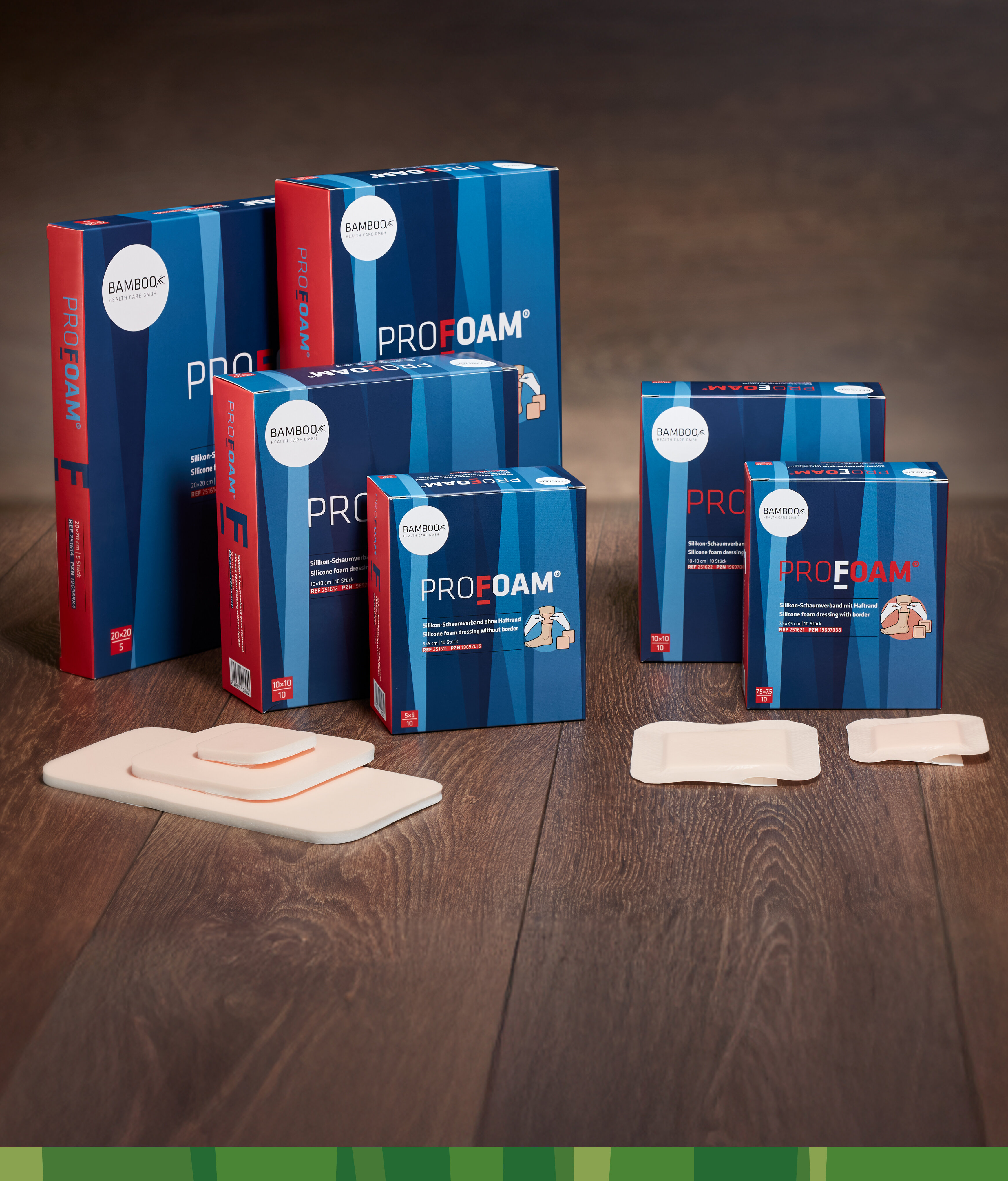 Alle sechs Verpackungsgrößen von ProFoam® mit und ohne Haftrand nebeneinander gestellt mit passendem Schaumverband im Vordergrund auf einem dunklen Holzboden. | © Bamboo Health Care GmbH