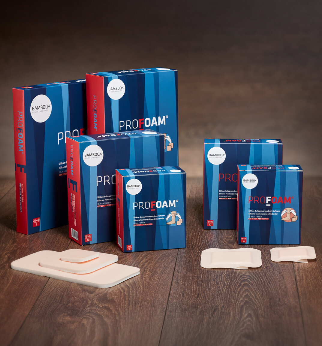 Die unterschiedlichen Verpackungsgrößen von ProFoam® mit einer Auswahl an ProFoam® Schaumverbänden im Vordergrund auf dunklem Holzboden. | © Bamboo Health Care GmbH