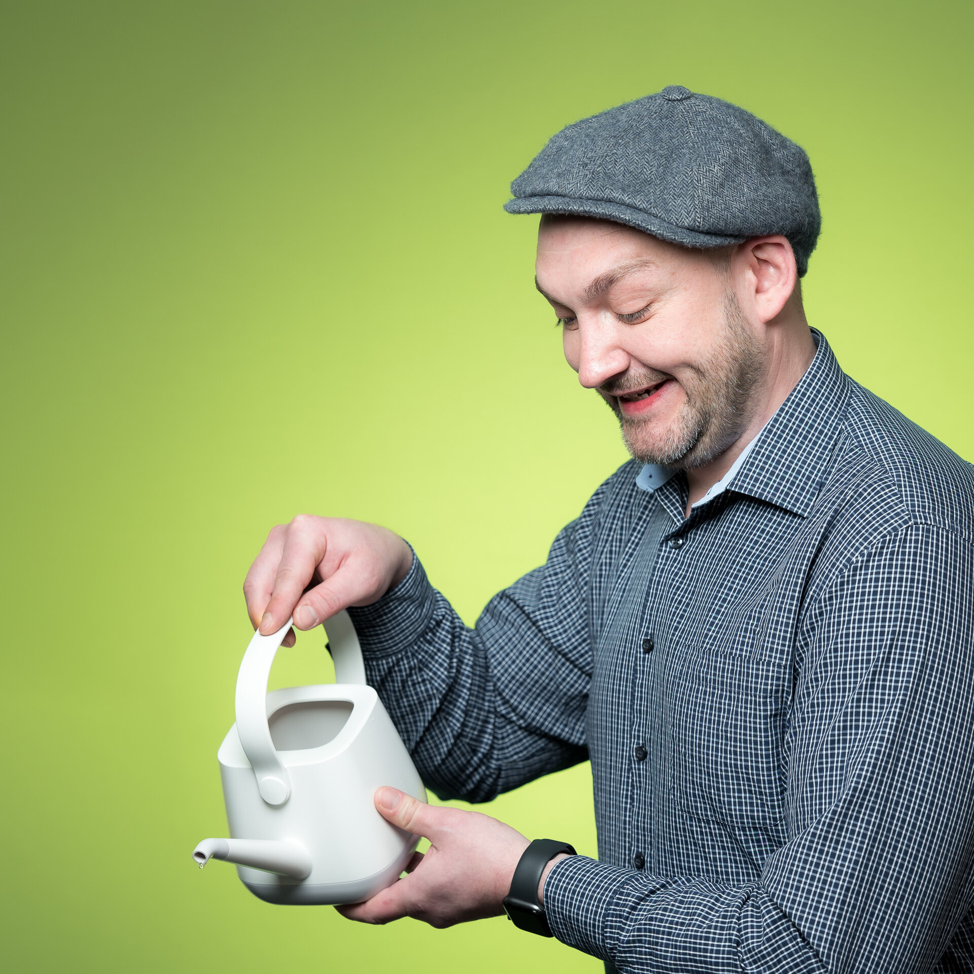 Kolja Schäfer hält lachend eine Gießkanne in der rechten Hand, stützt sie mit der linken und gießt nach unten. Dabei trägt er eine Schiebermütze. | © Bamboo Health Care GmbH