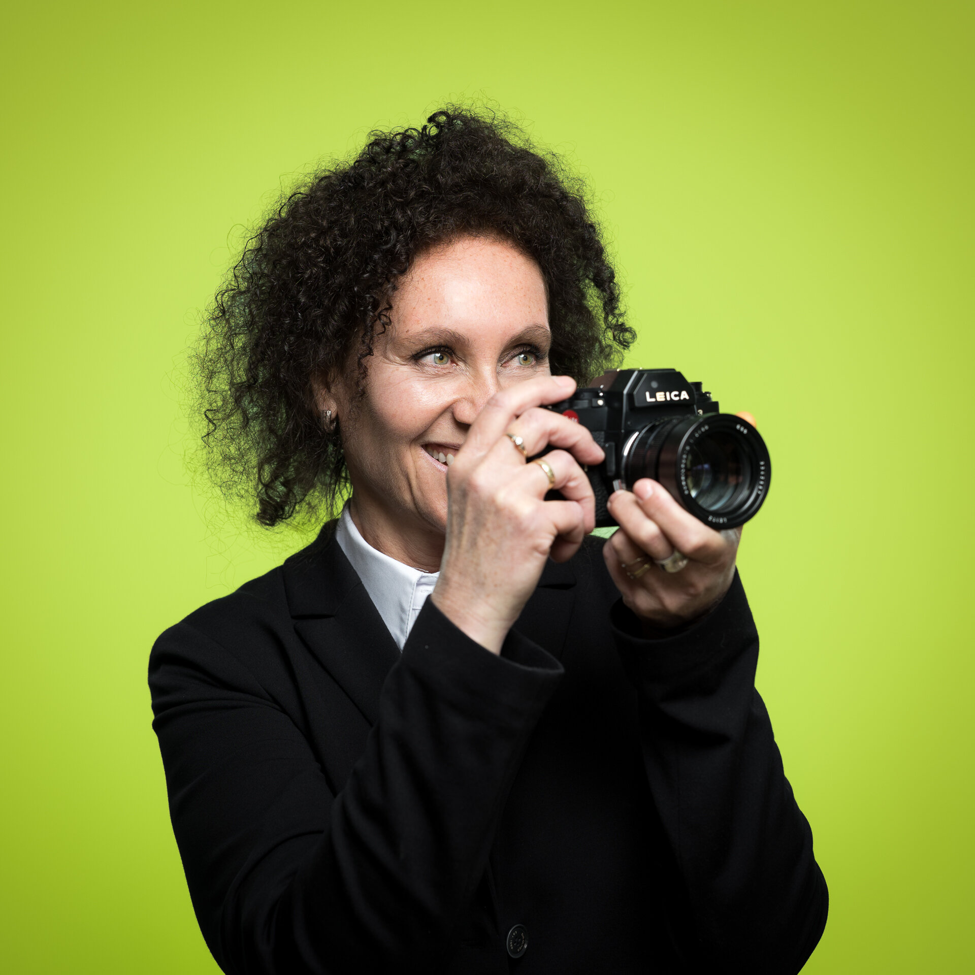 Evelyn Grafmüller schaut lächelnd durch den Sucher einer Leica-Kamera, die sie mit beiden Händen vor ihr Gesicht hält. | © Bamboo Health Care GmbH